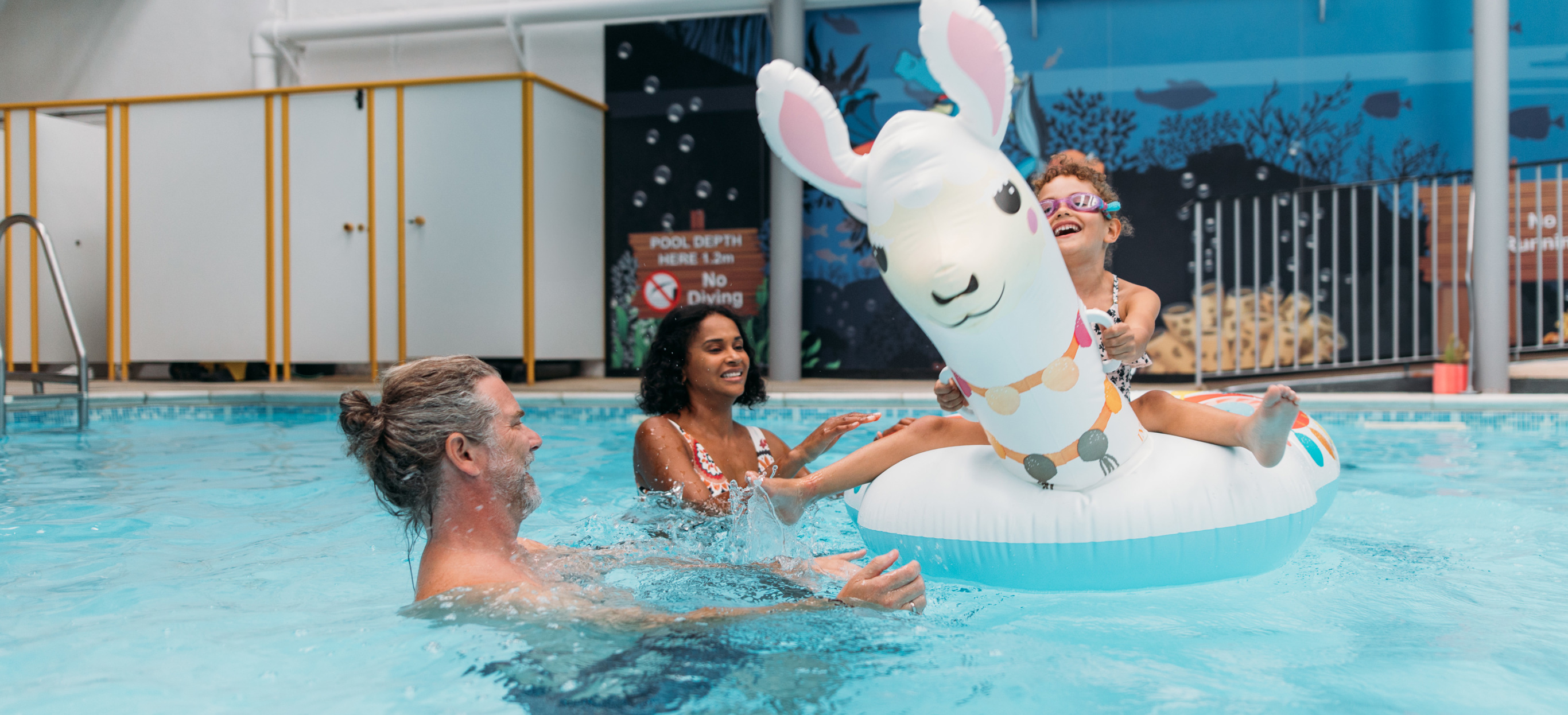 A couple with a young girl playing in an indoor heated swimming pool with pool floats