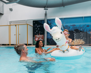 A couple with a young girl playing in an indoor heated swimming pool with pool floats