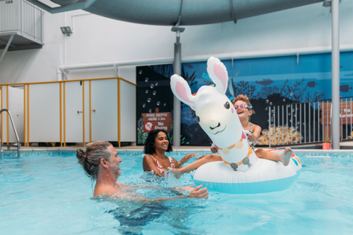 A couple with a young girl playing in an indoor heated swimming pool with pool floats
