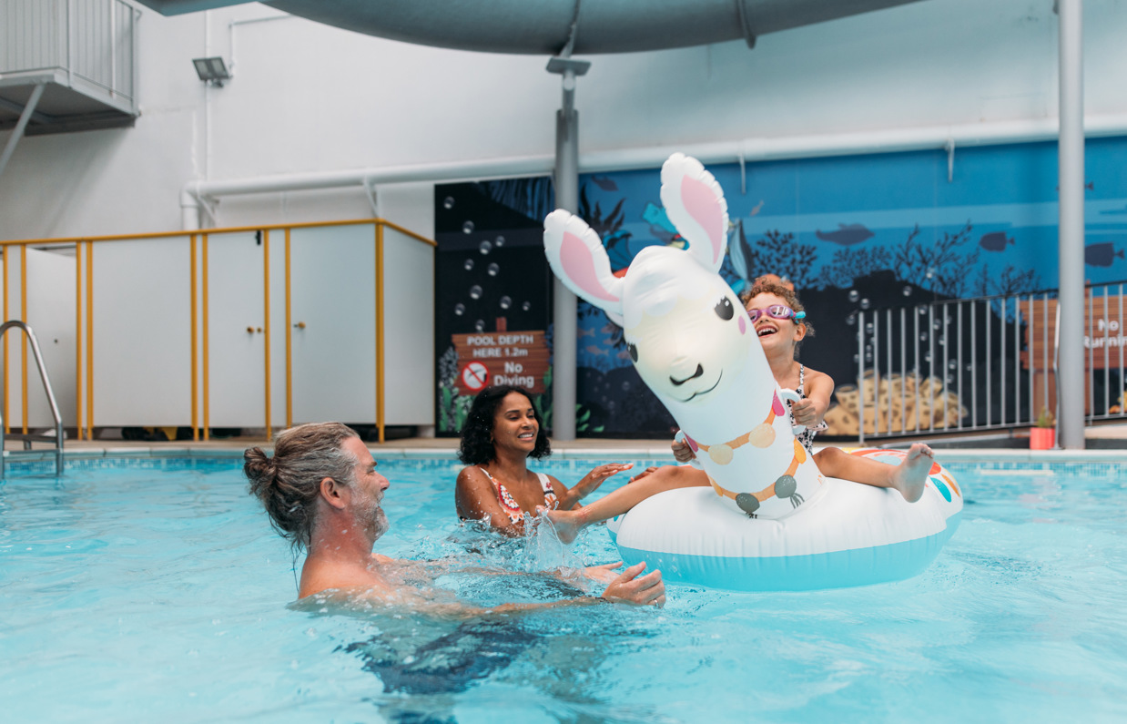 A couple with a young girl playing in an indoor heated swimming pool with pool floats