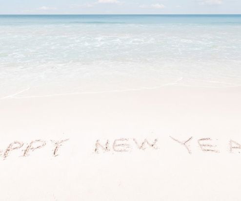 Happy New Year written in the sand at the beach with blue sea and sky in the background