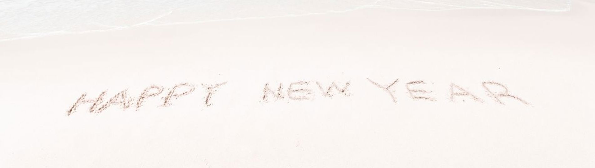 Happy New Year written in the sand at the beach with blue sea and sky in the background