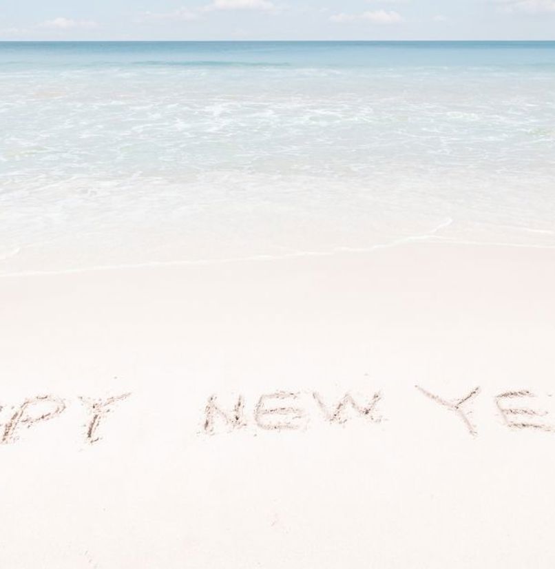 Happy New Year written in the sand at the beach with blue sea and sky in the background