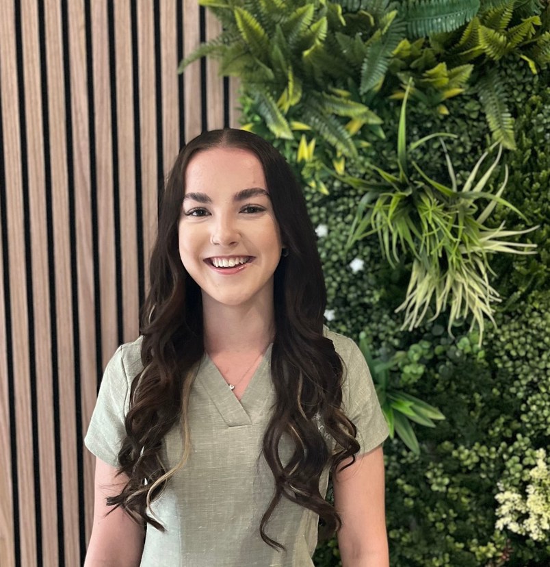 A lady smiling in spa uniform against a greenery / walnut decór background