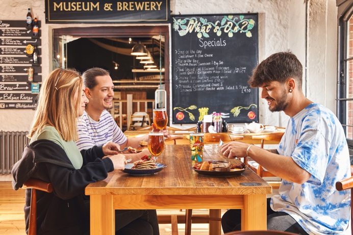 A group of people sat at a table in a brewery tap room enjoying food and drinks