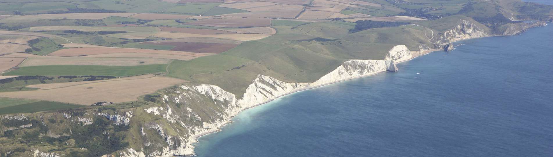 Aerial view of a stretch of the Jurassic Coast including blue sea, rugged cliffs and countryside