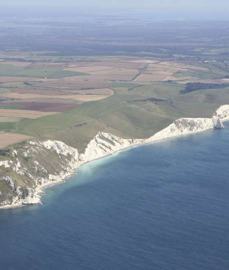 Aerial view of a stretch of the Jurassic Coast including blue sea, rugged cliffs and countryside