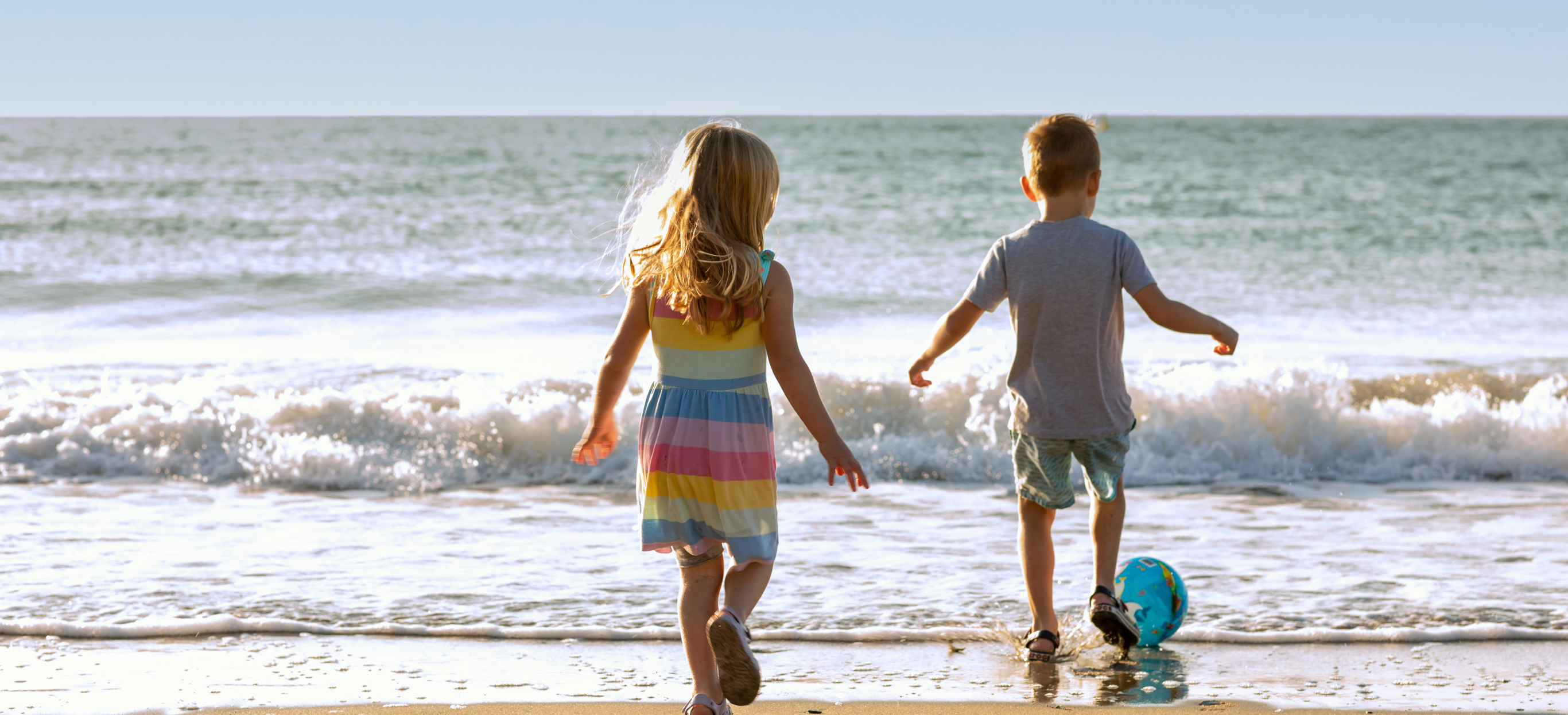 A young girl and boy playing with a ball on the beach by the sea at sunrise
