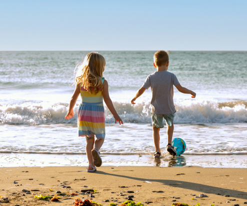 A young girl and boy playing with a ball on the beach by the sea at sunrise