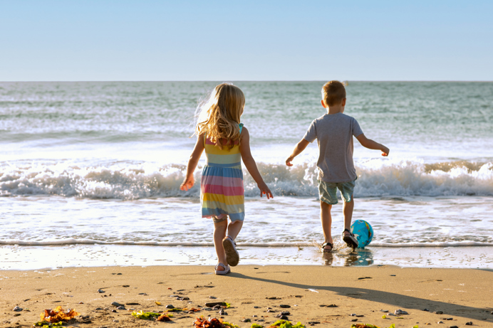 A young girl and boy playing with a ball on the beach by the sea at sunrise