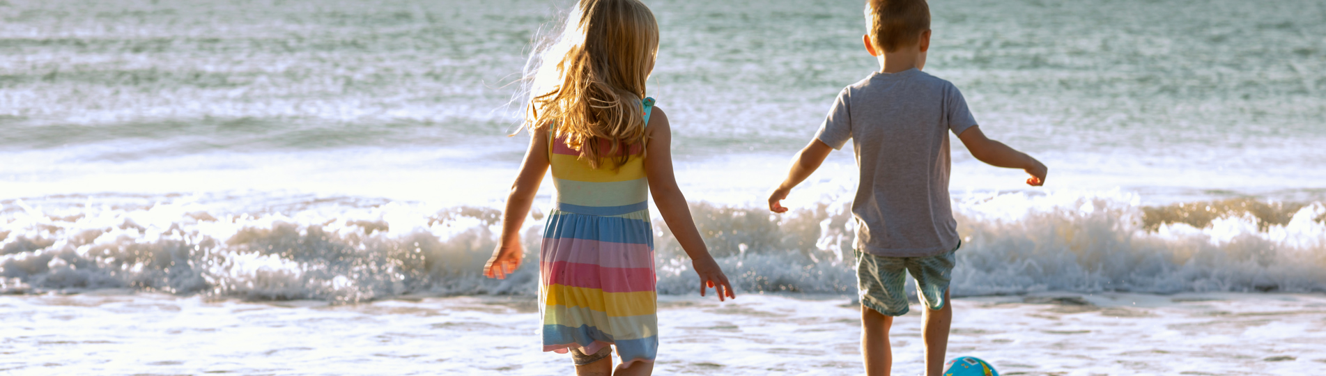A young girl and boy playing with a ball on the beach by the sea at sunrise