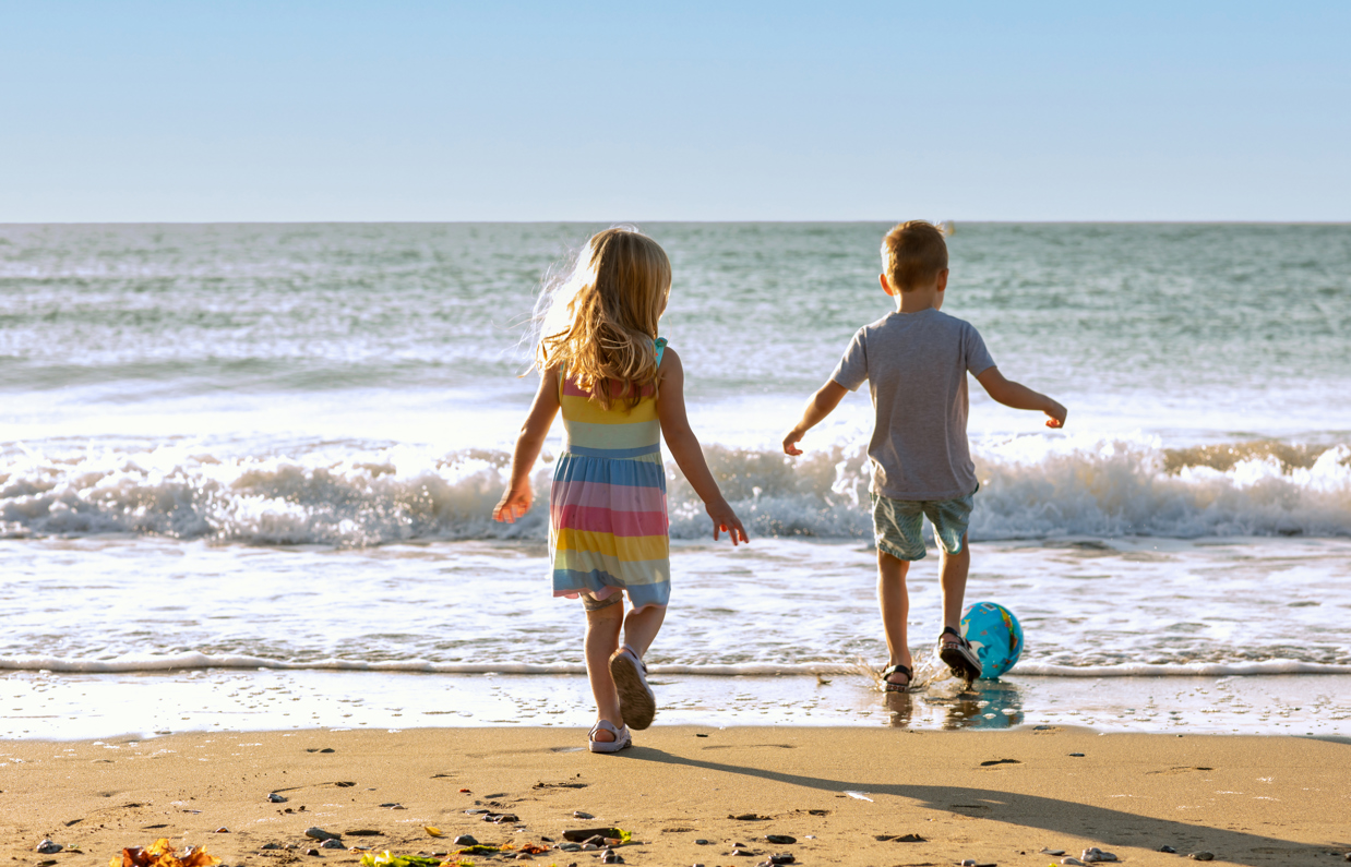 A young girl and boy playing with a ball on the beach by the sea at sunrise