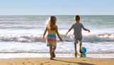 A young girl and boy playing with a ball on the beach by the sea at sunrise
