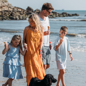 Family walking a dog on the beach eating ice creams