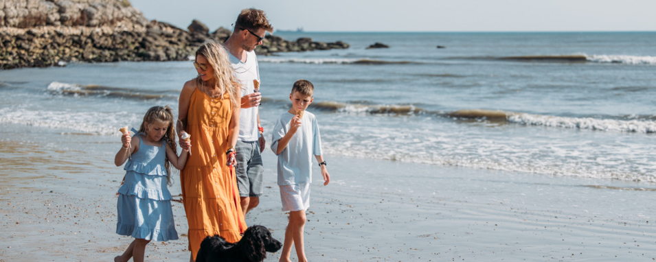 Family walking a dog on the beach eating ice creams