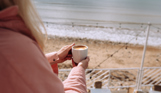 An over the shoulder shot of a woman looking out to sea from Drift Bar & Grill with a mug of coffee in her hands