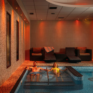A couple laid relaxing in a hydrotherapy spa pool with loungers to sit on and calm light