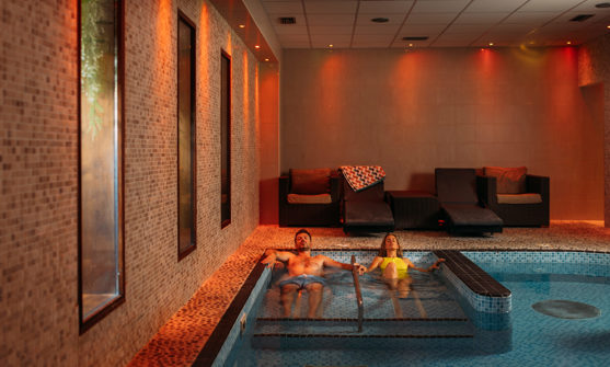 A couple laid relaxing in a hydrotherapy spa pool with loungers to sit on and calm light