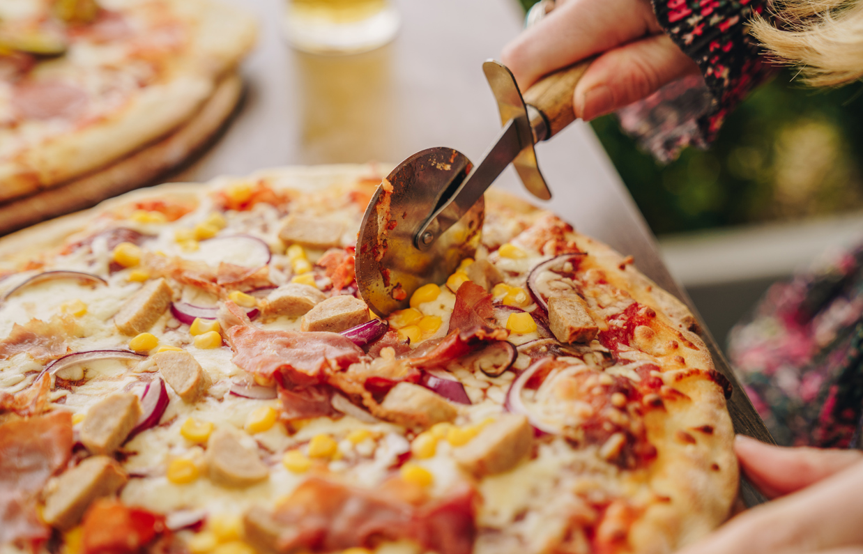 A pizza with various toppings being cut using a pizza knife