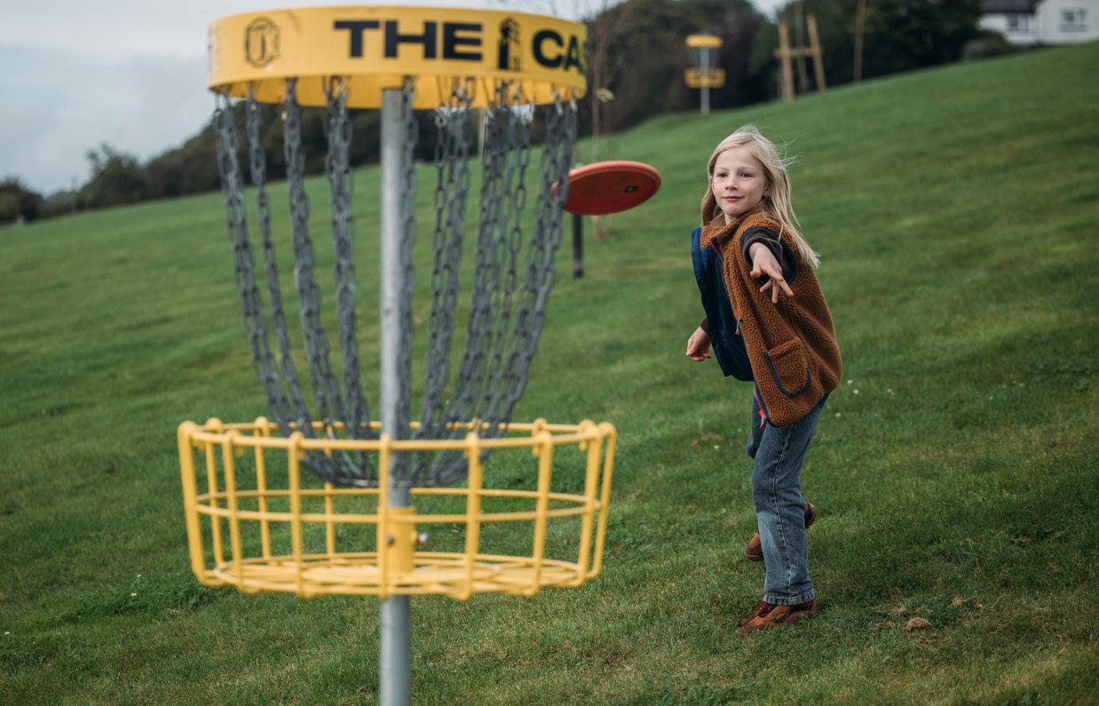 A young boy throwing a disc at the disc golf goal in a field