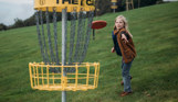 A young boy throwing a disc at the disc golf goal in a field
