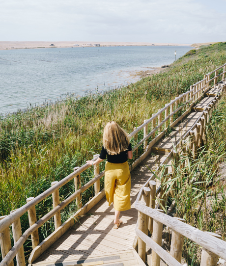 A woman with blonde hair walking along the coast path by Chesil Beach