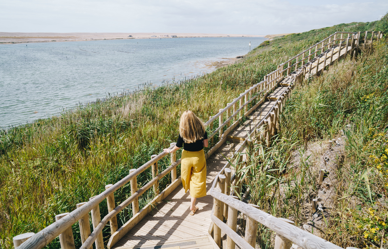A woman with blonde hair walking along the coast path by Chesil Beach