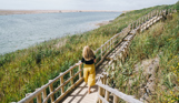 A woman with blonde hair walking along the coast path by Chesil Beach