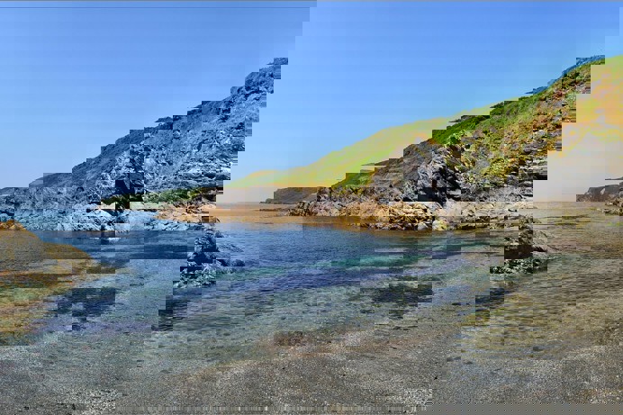 A small cove with rocky headland surrounding it on a sunny, blue sky day