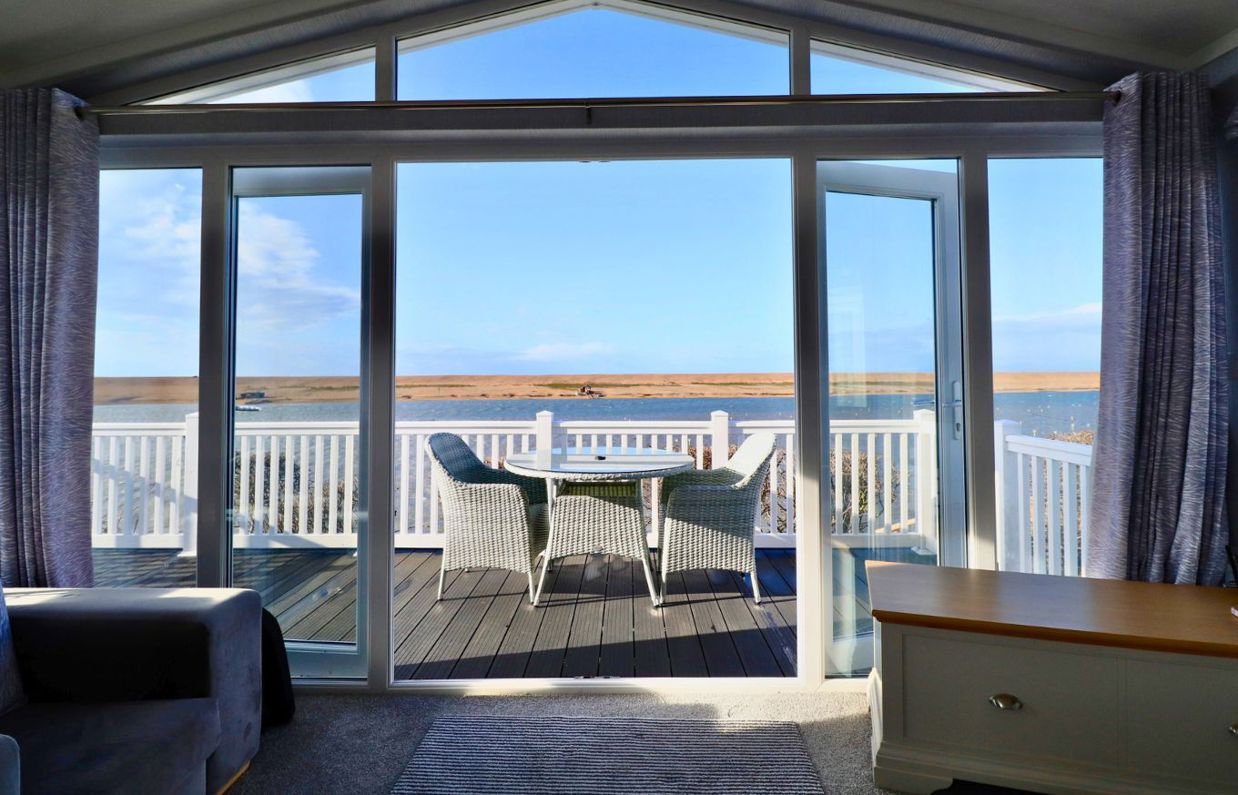 View looking out of caravan towards decking with outdoor furniture with sea and Chesil Beach in distance