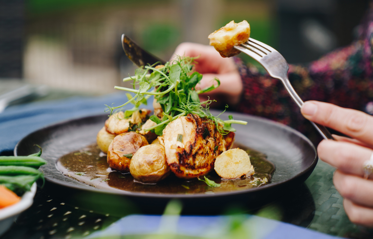 A meat and potato dish on a black plate being eaten outside at a table