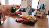 A woman sat at a table with a charcuterie board, pouring red wine into two wine glasses