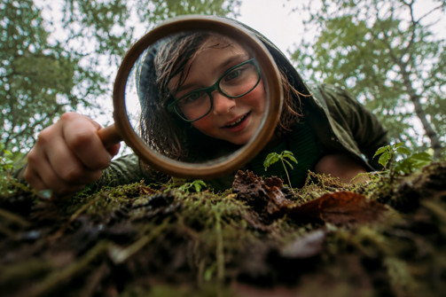 A young boy searching in the ground with a magnifying glass