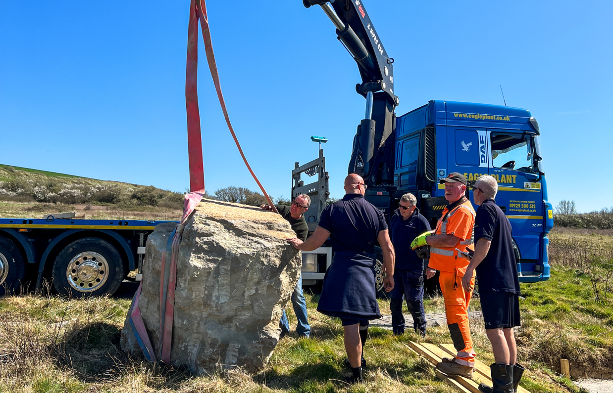 Installation of a stone sculpture in a field with blue skies