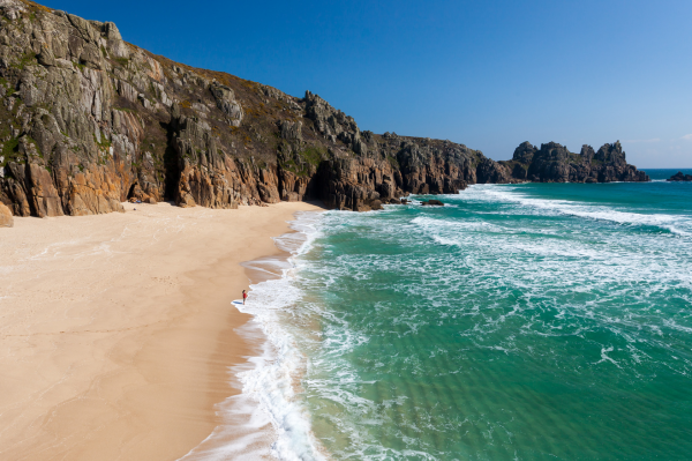 An idyllic beach with blue sea, a rocky cliff face and blue skies