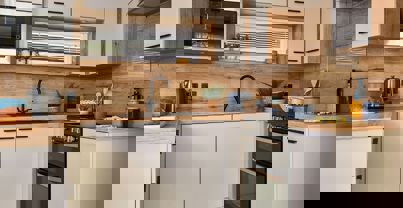 Contemporary kitchen with black fixtures, white units and natural wooden splashbacks and worktop