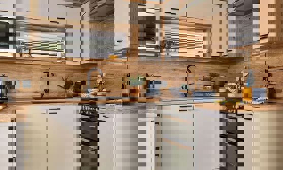 Contemporary kitchen with black fixtures, white units and natural wooden splashbacks and worktop