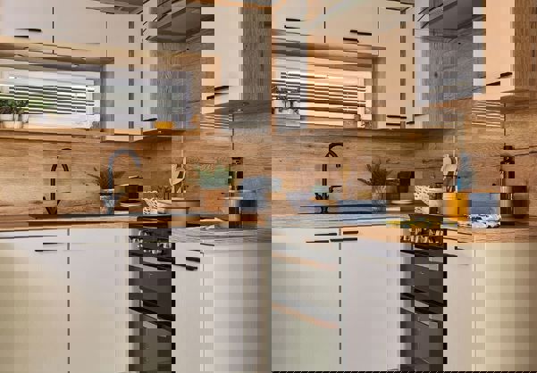 Contemporary kitchen with black fixtures, white units and natural wooden splashbacks and worktop