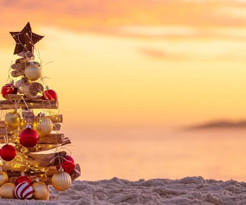 A driftwood christmas tree on sand at the beach with seaviews and striking orange and pink sky