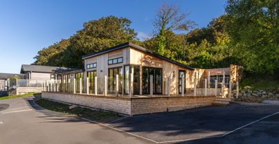 View of lodge from the South showing trees in background and large wraparound decking