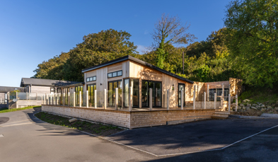 View of lodge from the South showing trees in background and large wraparound decking