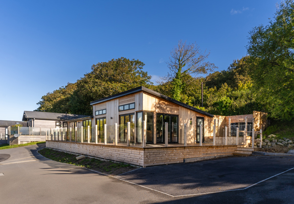 View of lodge from the South showing trees in background and large wraparound decking