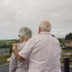 An older couple stood together on the decking of a holiday home looking out towards the view
