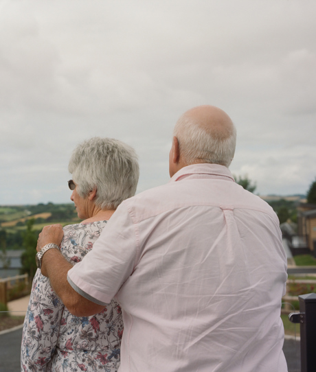 An older couple stood together on the decking of a holiday home looking out towards the view