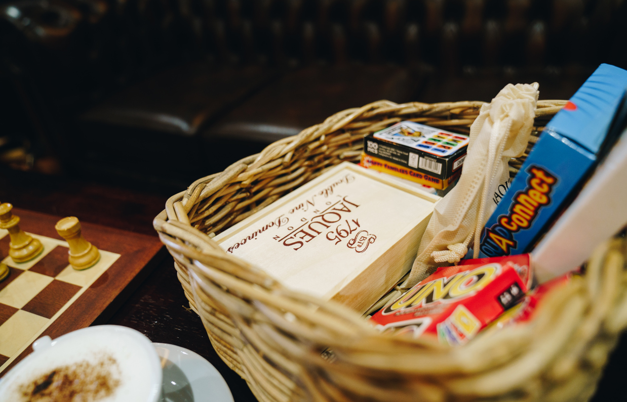 A wicker basket of various board and card games on a table next to a chess board and a coffee