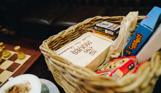 A wicker basket of various board and card games on a table next to a chess board and a coffee