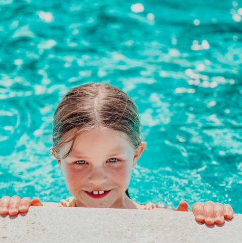 A young girl in a swimming pool with her hands holding onto the edge