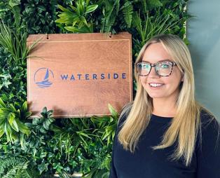 A smiling lady stood beside a Waterside sign
