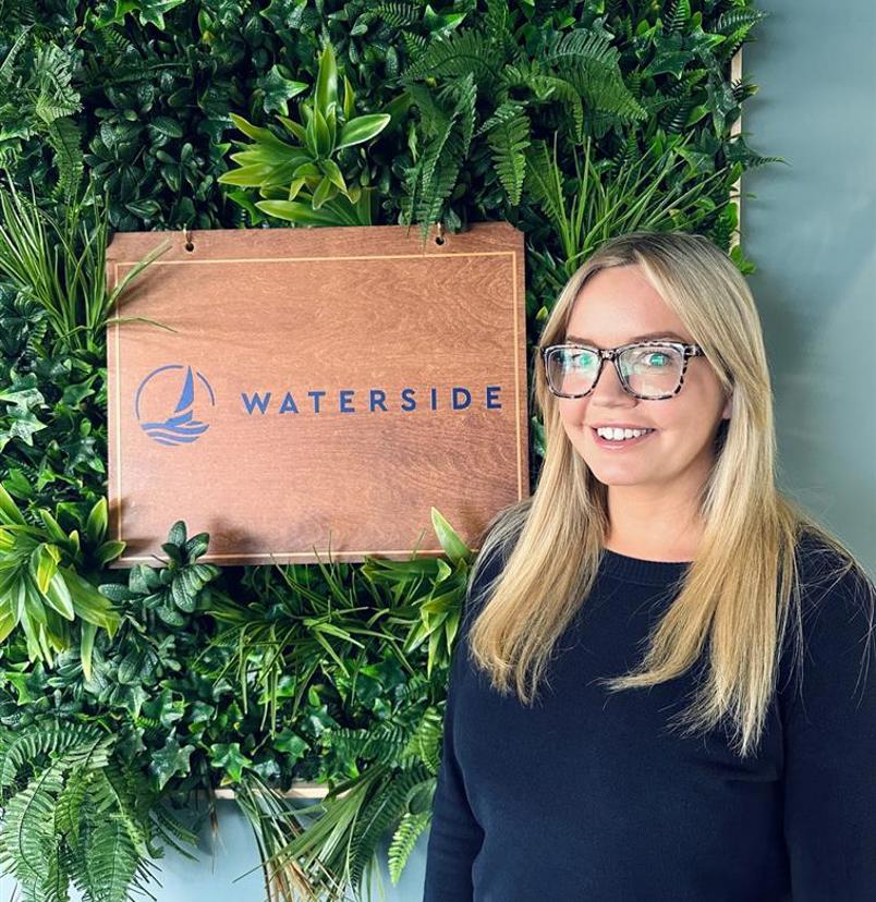 A smiling lady stood beside a Waterside sign