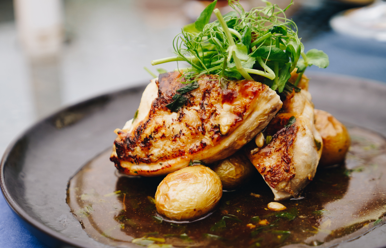 A meat dish on a black plate being eaten outside at a table